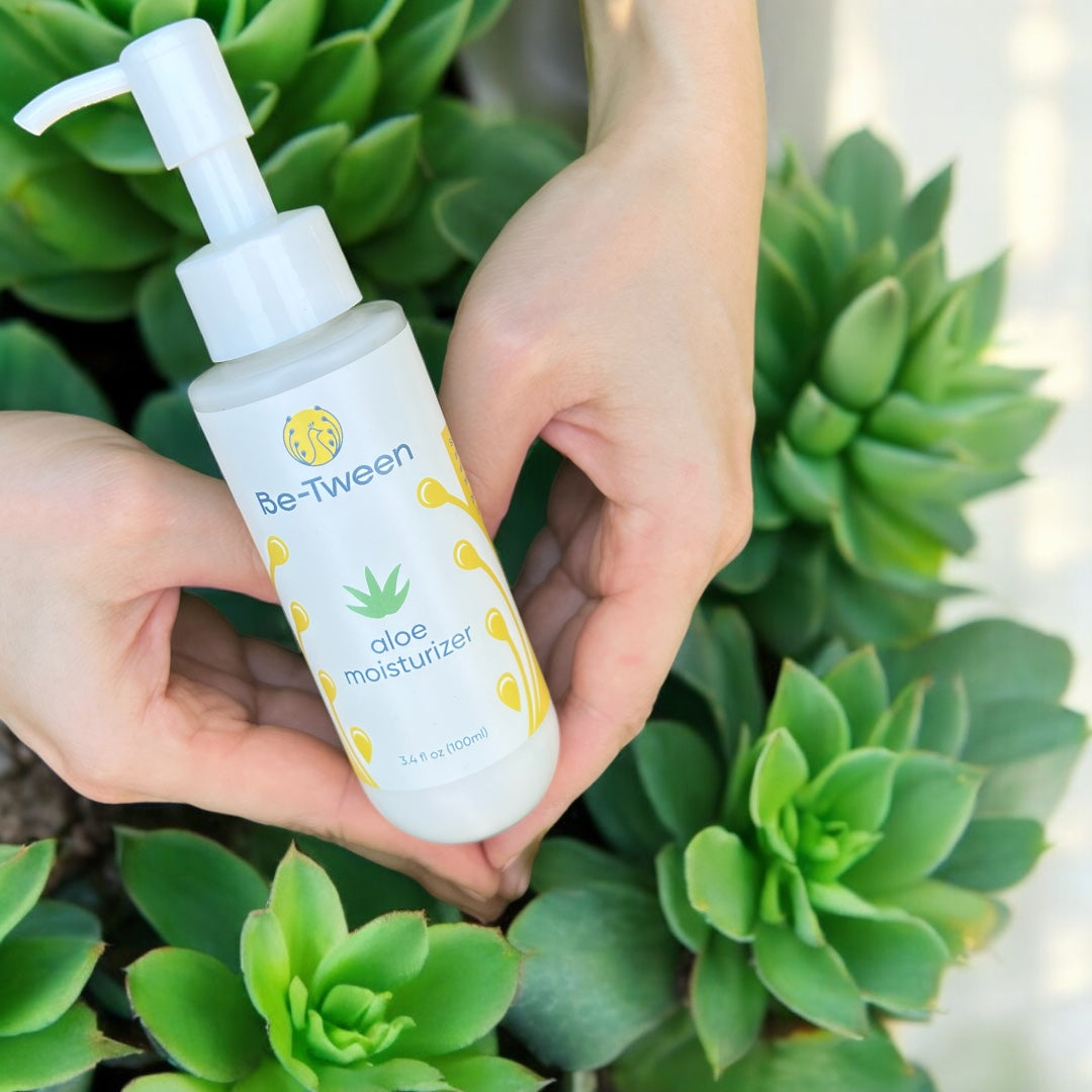 A hand shaped like a heart gently holding the Be-Tween Aloe Moisturizer, symbolizing care and love. Click to learn more about our story.